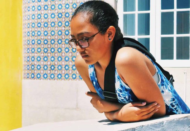 Jeune cap verdiennes observant des passants dans une rue typique de Lisbonne dont les façades sont couverts de faience ou d'azulejos.